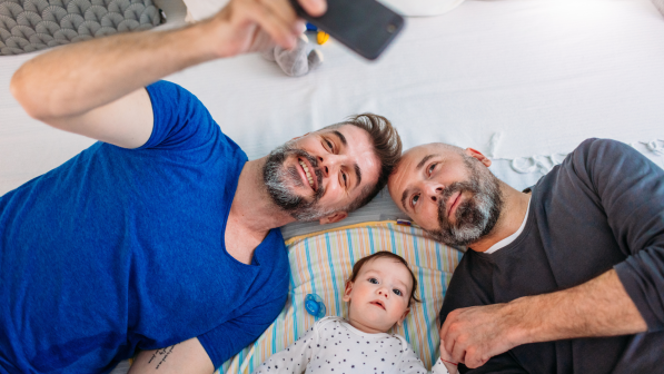 Two men lay on their backs taking a selfie with a baby. End HIV Nevada